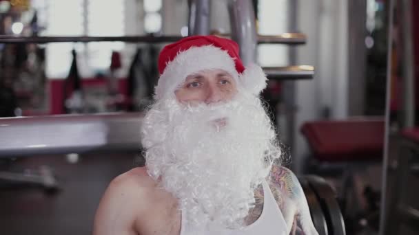 Instructor de fitness Santa Claus en el gimnasio entrena sus piernas en el simulador . — Vídeo de stock