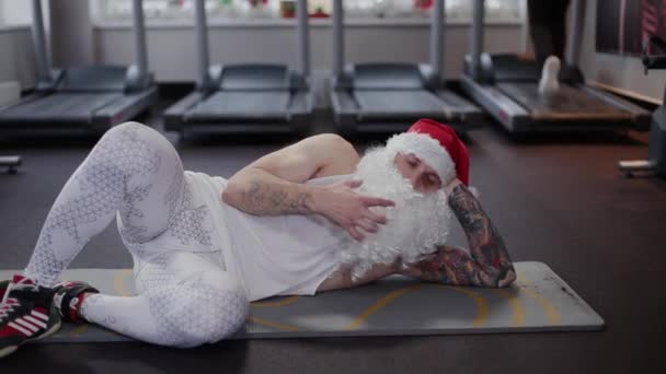 Instructor de fitness Santa Claus en el gimnasio descansando sobre la alfombra . — Vídeo de stock