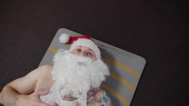 Fitness instructeur Santa Claus in de sportschool rusten op het tapijt. — Stockvideo