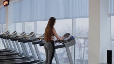 Çok güzel bir kadın spor salonunda bir koşu bandı üzerinde çalıştırmak için hazırlanıyor.