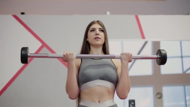 Mujer muy hermosa entrena bíceps con una barra en el gimnasio . — Vídeos de Stock