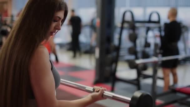 Mujer muy hermosa entrena bíceps con una barra en el gimnasio . — Vídeos de Stock