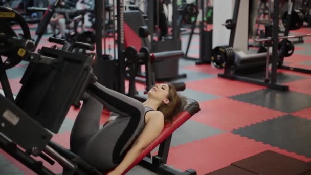 Mujer fitness muy hermosa entrena sus piernas en el simulador en el gimnasio . — Vídeos de Stock