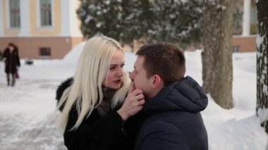Beautiful young couple sitting on a bench cuddle talking and smiling in a city winter park.