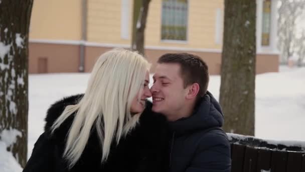 Красива молода пара сидить на лавці, розмовляє і посміхається в міському зимовому парку . — стокове відео