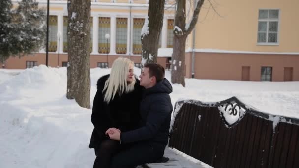 Beau jeune couple assis sur un banc câlin parlant et souriant dans un parc d'hiver de la ville . — Video