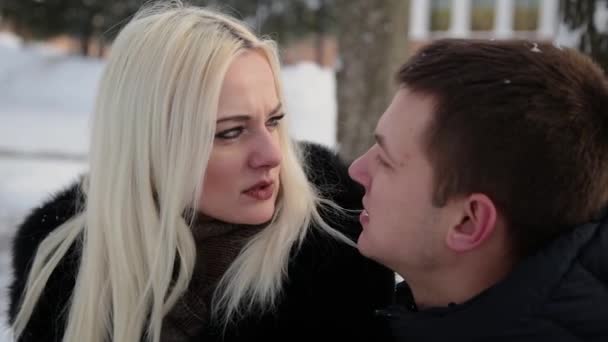 Beautiful young couple sitting on a bench cuddle talking and smiling in a city winter park. — 图库视频影像