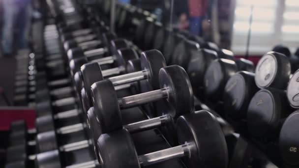 Handsome sporty man picks up dumbbells from the racks in the gym. — Stock Video