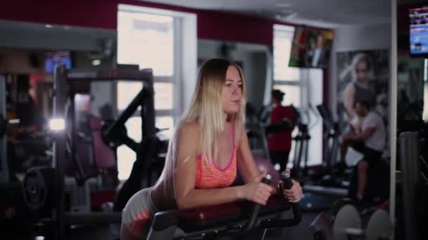 Very beautiful and sexy fitness model trains back thigh on a gym machine in the gym. — Stock Video