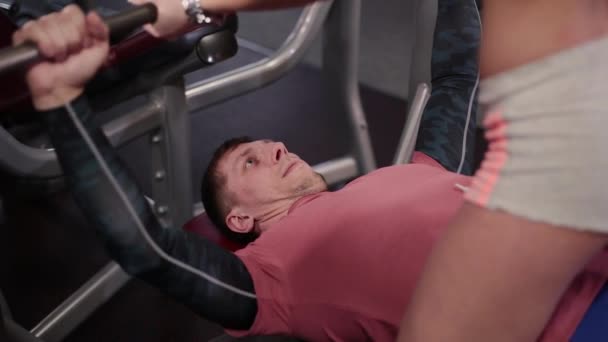 Очень красивая и сексуальная фитнес-модель помогает выполнять жим лежа мужчине в тренажерном зале . — стоковое видео