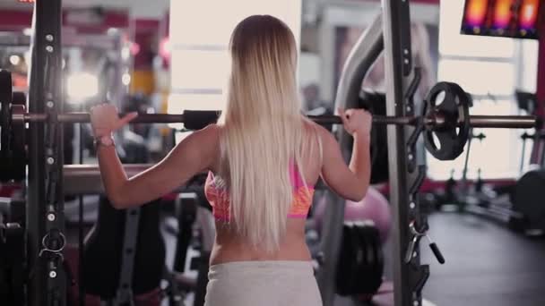 Modelo de fitness muy hermoso y sexy entrena las piernas con una barra atlética en el gimnasio . — Vídeos de Stock