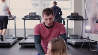 Atletik ve çekici bir adam spor salonunda yerde germek için güzel bir kadın yardımcı olur..