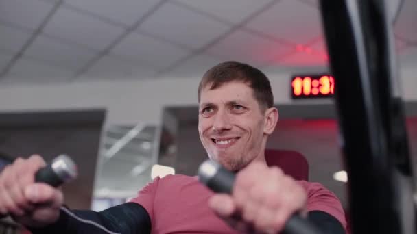 Atletisk och attraktiv man tränar bröstmusklerna på en simulator i gymmet. — Stockvideo