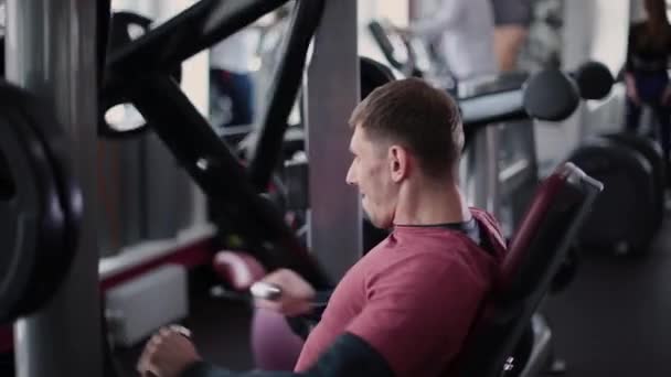 Atletisk och attraktiv man tränar bröstmusklerna på en simulator i gymmet. — Stockvideo