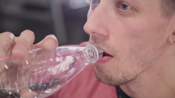 Atletische en aantrekkelijke man drinking water uit een fles in de sportschool. — Stockvideo