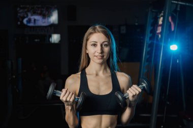 Genç ve güzel kadın spor salonunda dumbbells ile çalışma dışarı. Pazı bukleler.