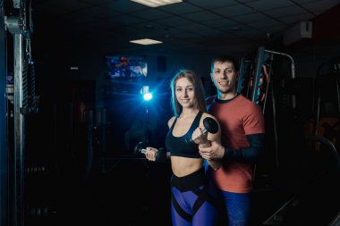 Aktif güzel fitness modeli kız pazı dumbbells ile birlikte spor salonunda bir eğitmen ile trenler.