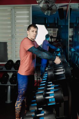 Yakışıklı atletik erkek dumbbells raflar daha fazla eğitim için gelen spor salonunda alır..