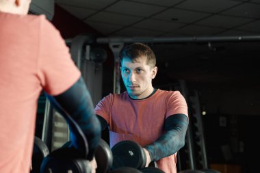 Yakışıklı atletik erkek dumbbells raflar daha fazla eğitim için gelen spor salonunda alır..