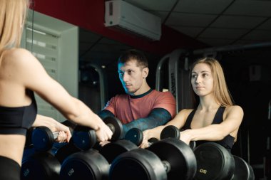 Aktif güzel fitness modeli kız ve atletik erkek spor salonunda dumbbells raflar üzerinden al.