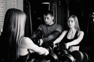 Aktif güzel fitness modeli kız ve atletik erkek spor salonunda dumbbells raflar üzerinden al.