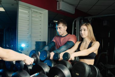 Aktif güzel fitness modeli kız ve atletik erkek spor salonunda dumbbells raflar üzerinden al.