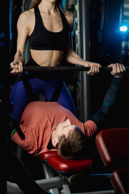 Kadın eğitmen adam salonda Bar Bench Press eğitmek için yardım.