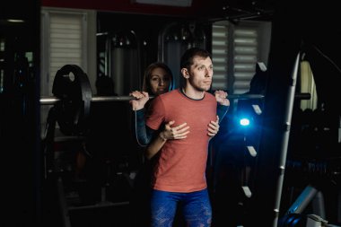 Spor salonunda atletik bir adam çömelme üzerinde aktif güzel fitness modeli kız ısrar ediyor.