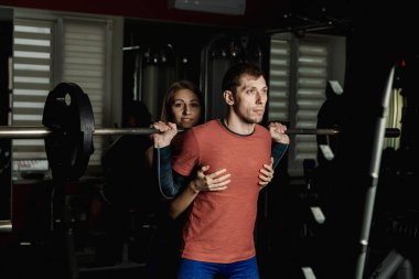 Spor salonunda atletik bir adam çömelme üzerinde aktif güzel fitness modeli kız ısrar ediyor.