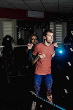 Spor salonunda atletik bir adam çömelme üzerinde aktif güzel fitness modeli kız ısrar ediyor.