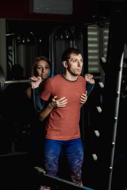 Spor salonunda atletik bir adam çömelme üzerinde aktif güzel fitness modeli kız ısrar ediyor.