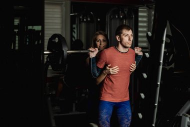 Spor salonunda atletik bir adam çömelme üzerinde aktif güzel fitness modeli kız ısrar ediyor.