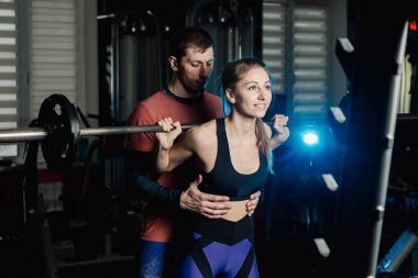 Yakışıklı atletik adam güzel bir kız için hiç bir şey ile bir halter salonunda omuzlarında yardımcı olur.