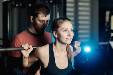 Yakışıklı atletik adam güzel bir kız için hiç bir şey ile bir halter salonunda omuzlarında yardımcı olur.