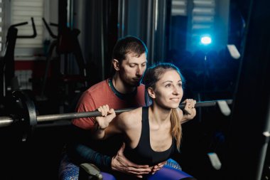 Yakışıklı atletik adam güzel bir kız için hiç bir şey ile bir halter salonunda omuzlarında yardımcı olur.