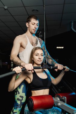 Yakışıklı atletik adam güzel bir kız bloğu simülatör spor salonunda tren yardımcı olur..
