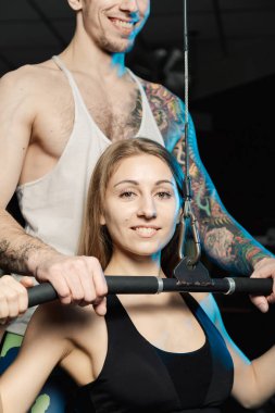 Yakışıklı atletik adam güzel bir kız bloğu simülatör spor salonunda tren yardımcı olur..