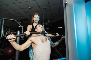 Aktif güzel fitness modeli kız Genç adam blok simülatör spor salonunda tren yardımcı olur..