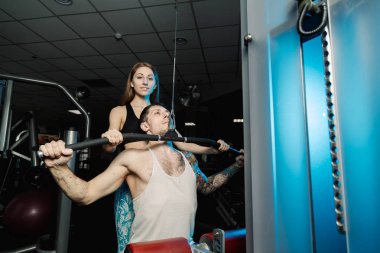 Aktif güzel fitness modeli kız Genç adam blok simülatör spor salonunda tren yardımcı olur..