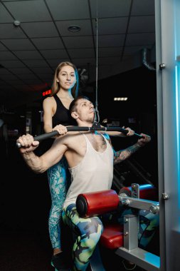 Aktif güzel fitness modeli kız Genç adam blok simülatör spor salonunda tren yardımcı olur..