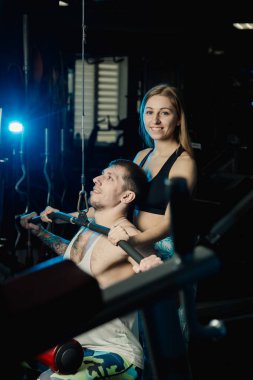 Aktif güzel fitness modeli kız Genç adam blok simülatör spor salonunda tren yardımcı olur..