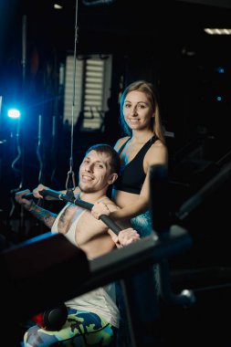 Aktif güzel fitness modeli kız Genç adam blok simülatör spor salonunda tren yardımcı olur..