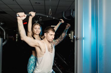 Aktif güzel fitness modeli kız Genç adam blok simülatör spor salonunda tren yardımcı olur..