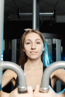 Aktif güzel fitness modeli kız göğüs kasları bir simülatör spor salonunda trenler.