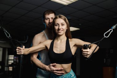 Simülatör spor salonunda bir eğitmen ile birlikte göğüs kasları aktif güzel fitness modeli kız trenler.