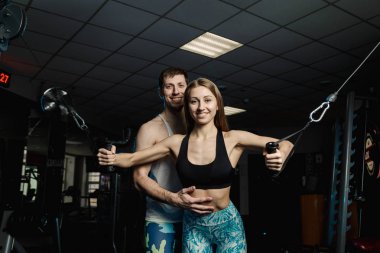 Simülatör spor salonunda bir eğitmen ile birlikte göğüs kasları aktif güzel fitness modeli kız trenler.