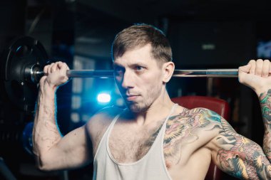 Yakışıklı atletik spor salonunda bankta oturmuş halter kaldırma omuz trenler.