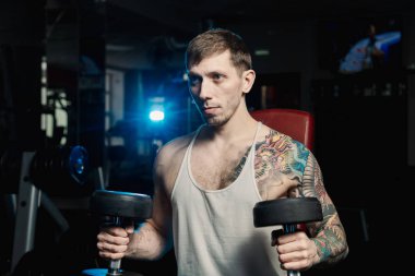 Spor salonunda bir bankta oturmuş dumbbells ile omuzlarını eğitim yakışıklı atletik erkek.