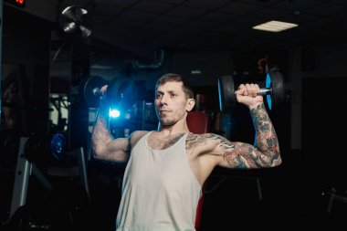 Spor salonunda bir bankta oturmuş dumbbells ile omuzlarını eğitim yakışıklı atletik erkek.