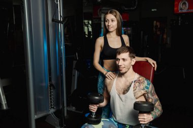 Aktif güzel fitness modeli kız erkek spor salonunda otururken dumbbells ile tren yardımcı olur.